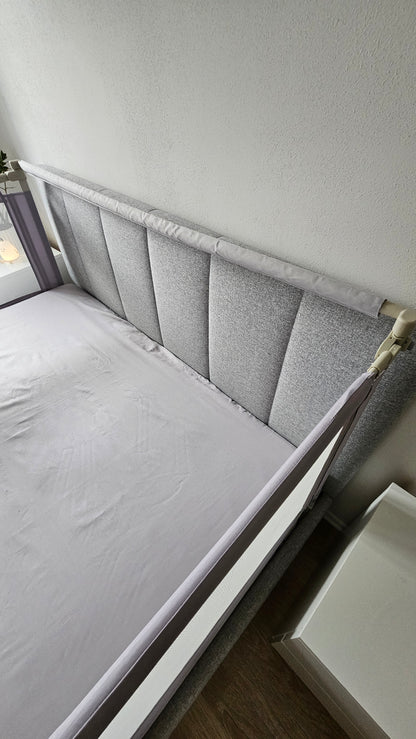 Gray upholstered bed with padded headboard and safety rail in modern bedroom