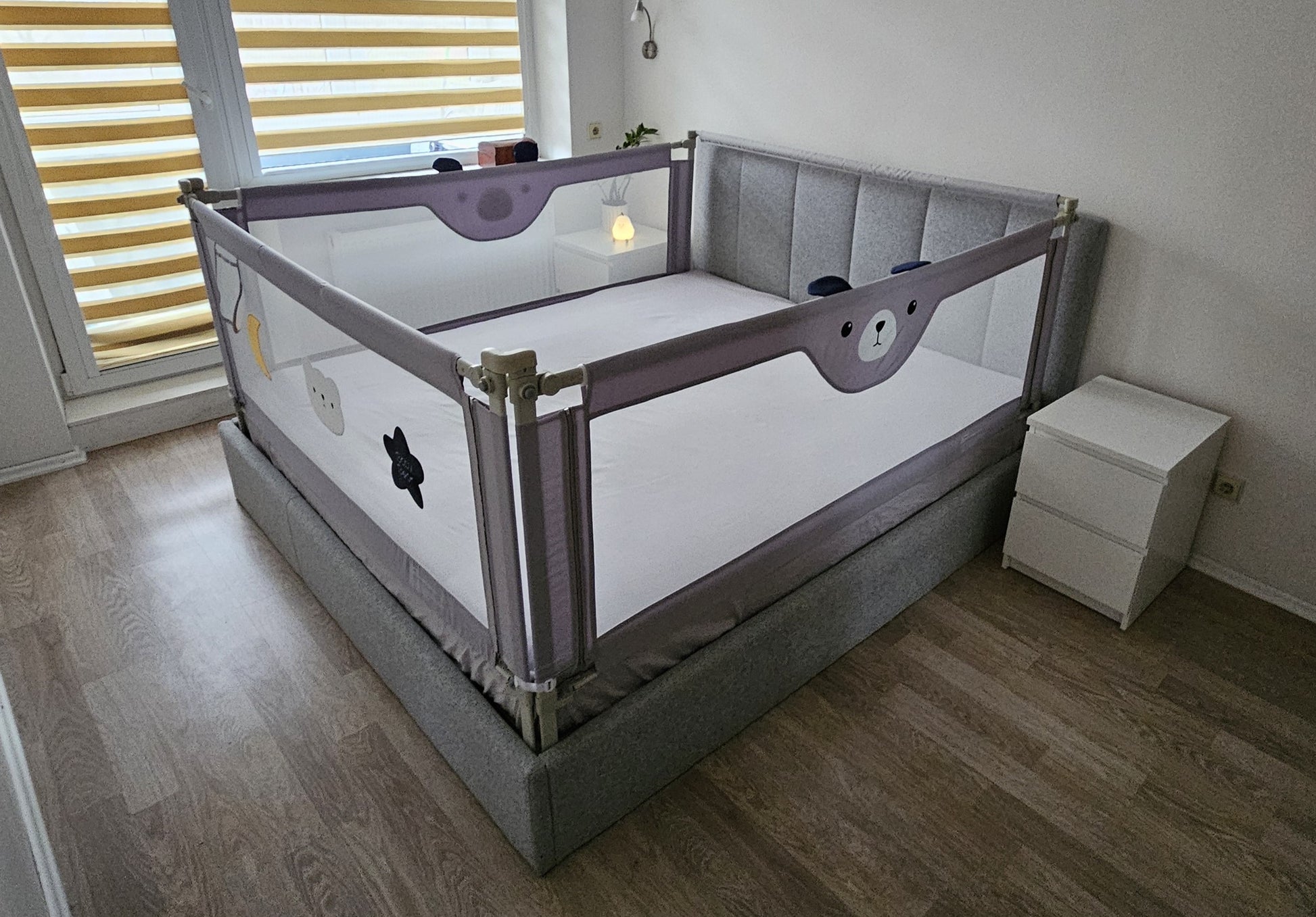 Gray upholstered bed with child safety rails in a modern bedroom with wooden floor