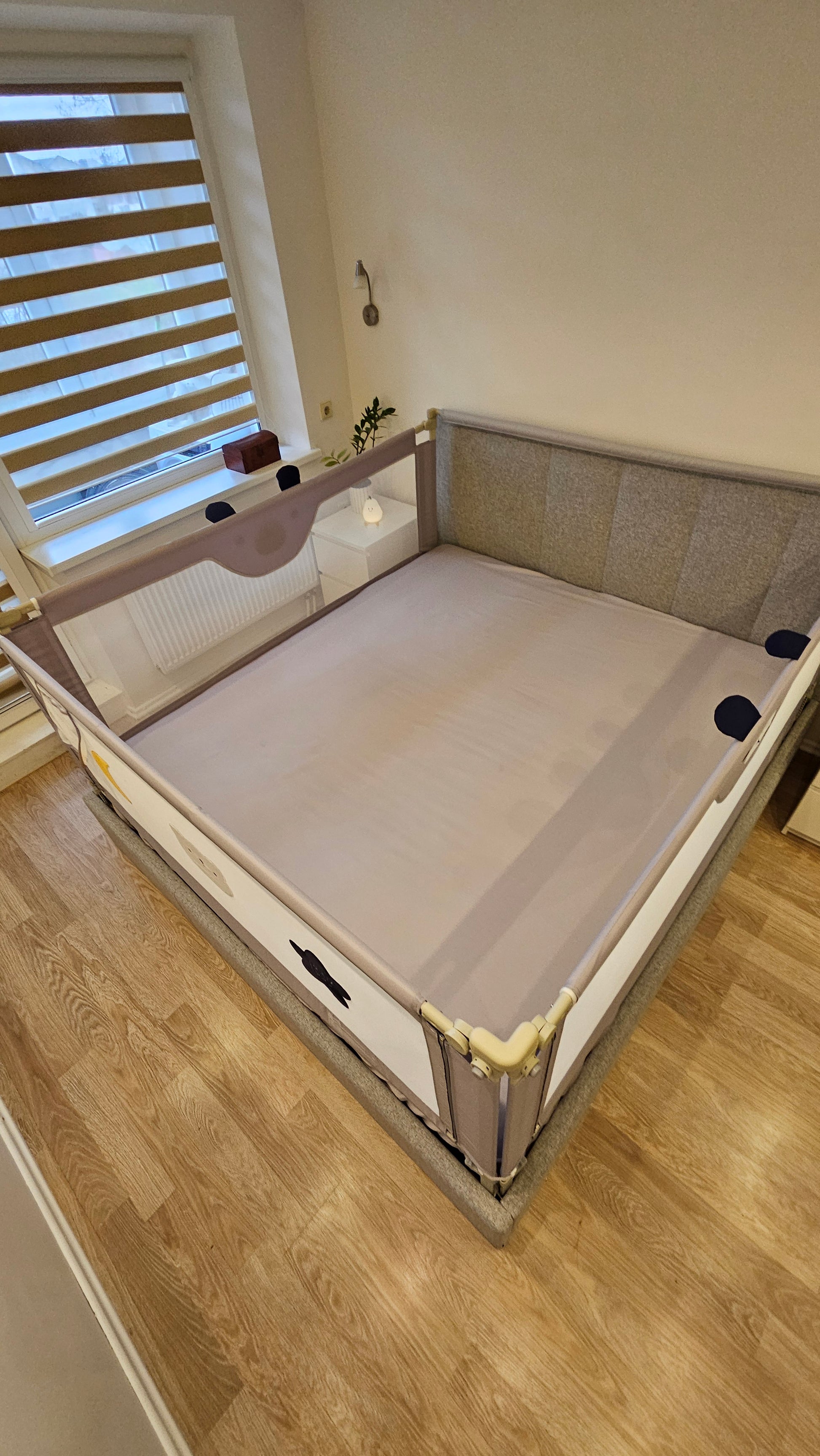 Large upholstered bed with gray safety rails in a bright bedroom with wood flooring