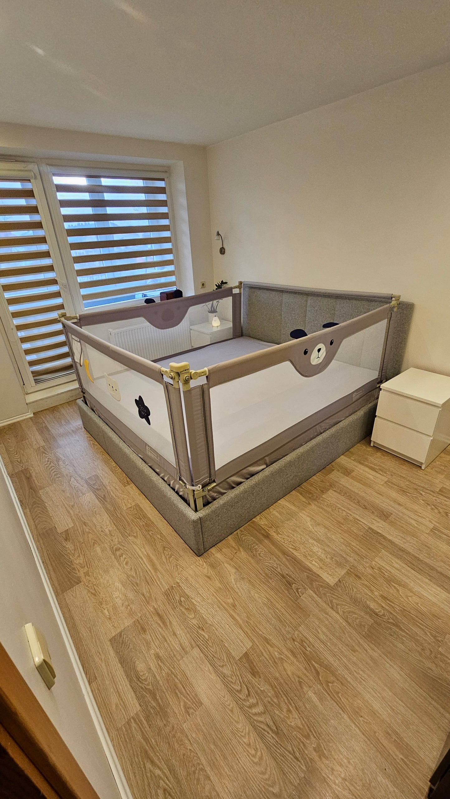Gray toddler bed with animal-themed safety rail in a modern nursery with wood floor