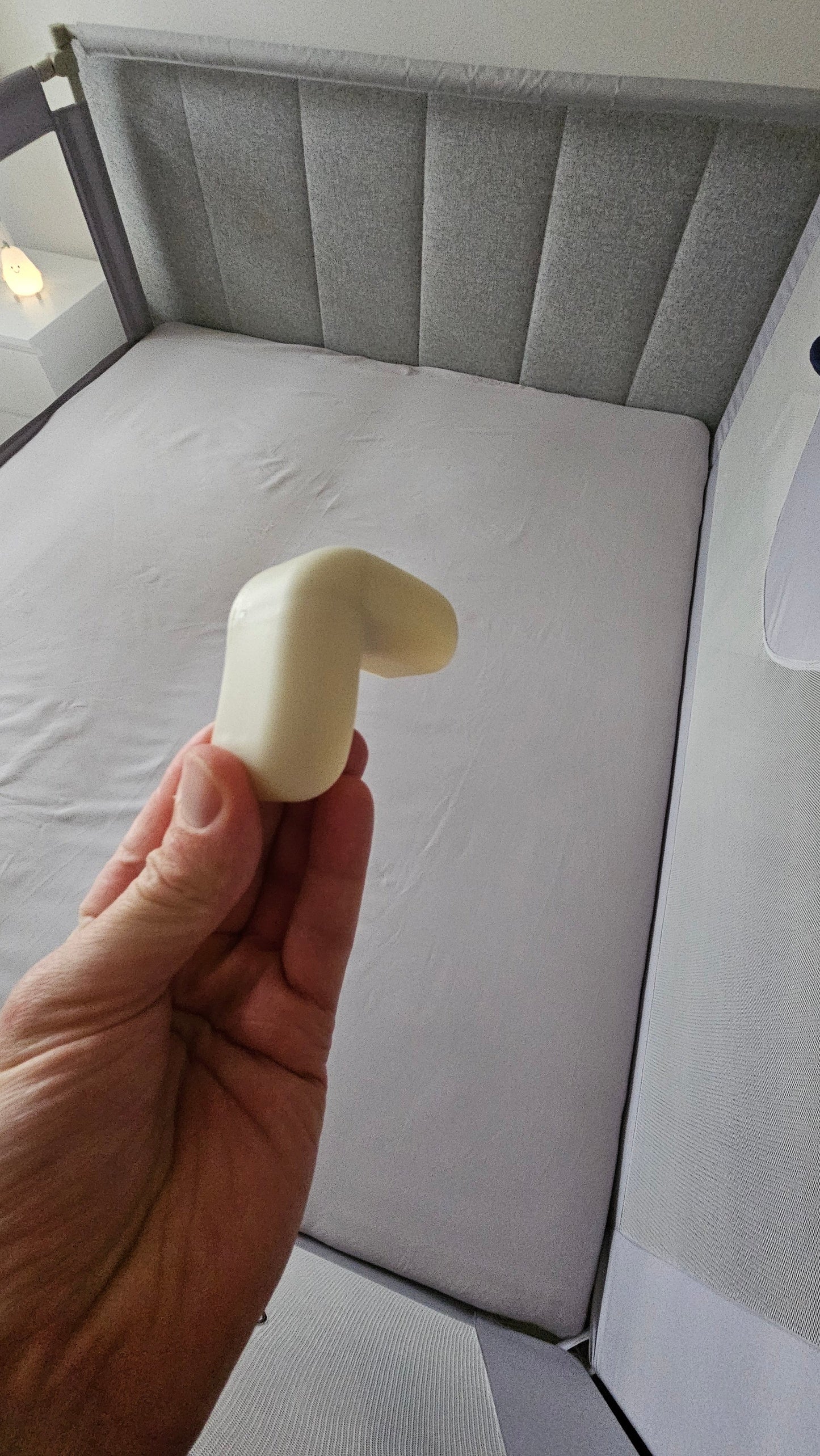 Hand holding corner protector above grey baby crib with mesh sides