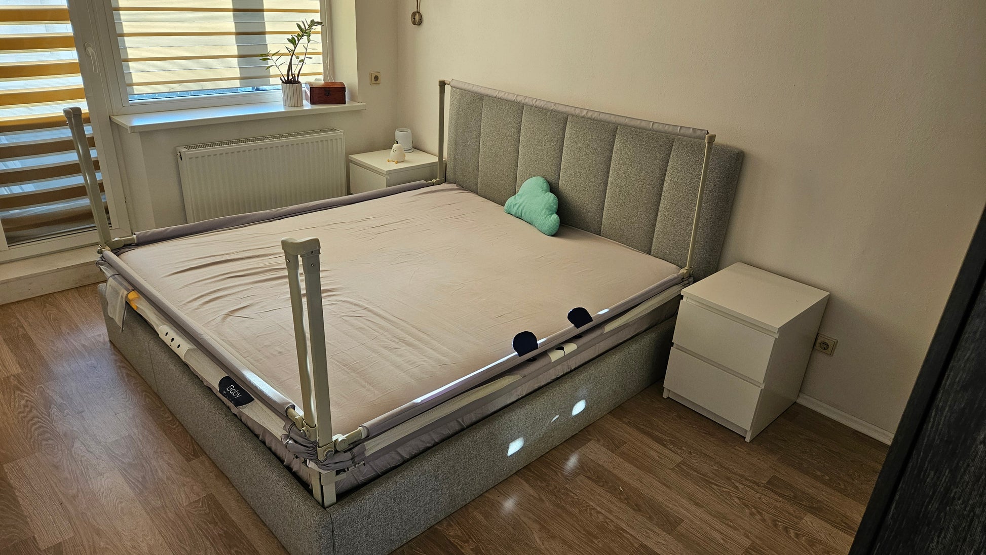 Modern bedroom with grey upholstered bed, safety bed rail, cloud pillow and wooden floor